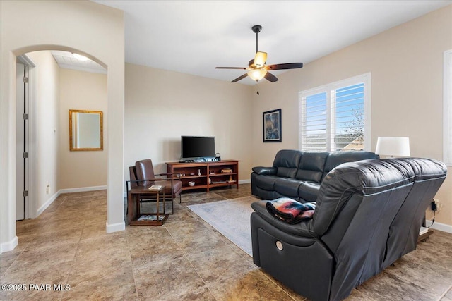 living room featuring baseboards, arched walkways, and ceiling fan