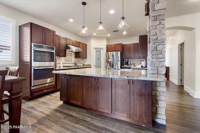 6969 E Encampment Dr, Prescott Valley, AZ 86314 - kitchen featuring hanging light fixtures, stainless steel appliances, light stone counters, a center island with sink, and decorative backsplash