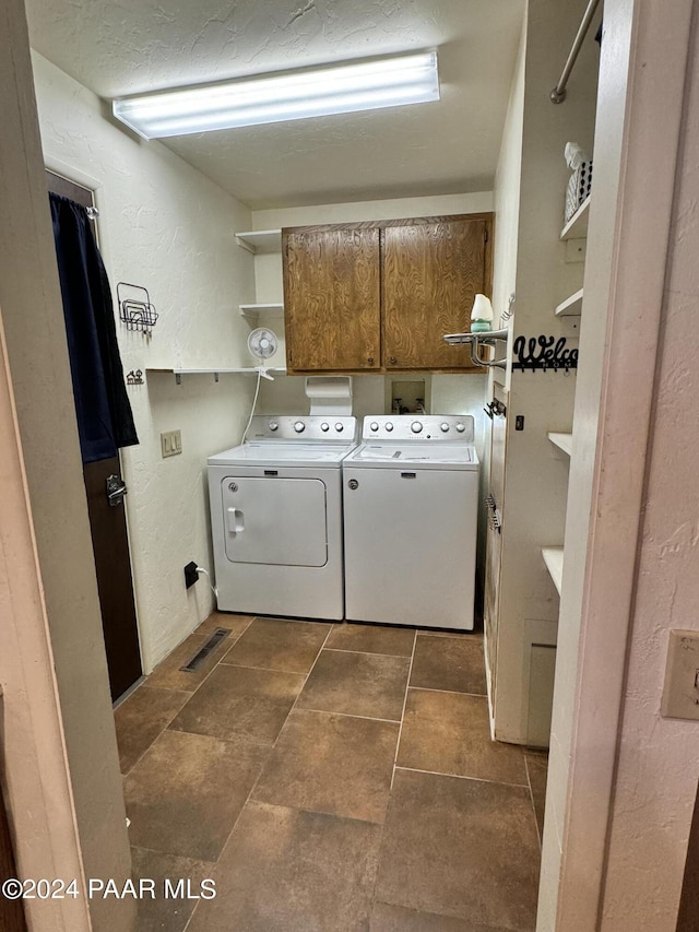 laundry area with washing machine and clothes dryer, cabinets, and dark tile patterned flooring