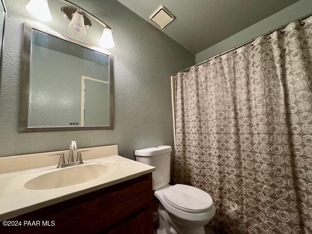 bathroom featuring a textured wall, toilet, vanity, lofted ceiling, and curtained shower