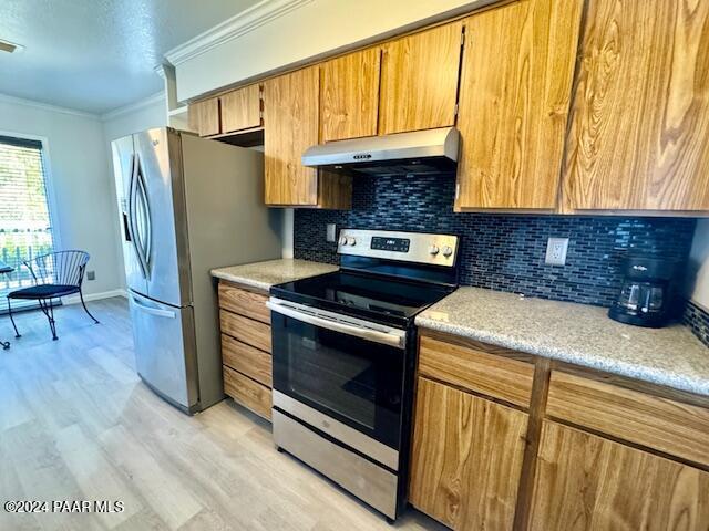 kitchen featuring appliances with stainless steel finishes, under cabinet range hood, ornamental molding, light wood-style flooring, and decorative backsplash