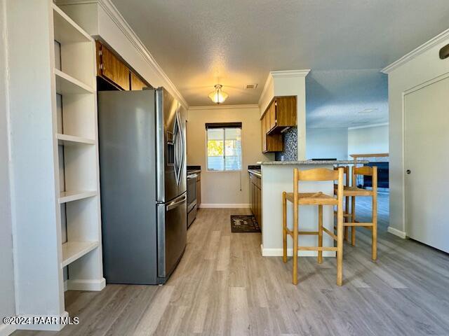 kitchen with stainless steel appliances, brown cabinetry, light wood-style floors, crown molding, and a breakfast bar