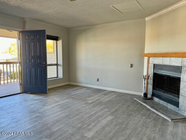 unfurnished living room with ornamental molding, wood finished floors, a textured ceiling, a fireplace, and baseboards