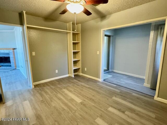 unfurnished bedroom featuring a textured ceiling, wood finished floors, baseboards, a tiled fireplace, and a ceiling fan