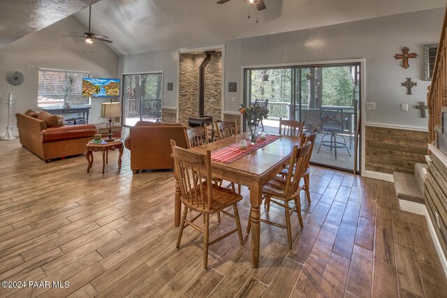 dining space featuring a wood stove, ceiling fan, wood-type flooring, and lofted ceiling