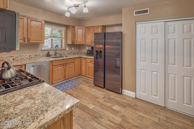 kitchen featuring light stone counters, a textured ceiling, stainless steel appliances, sink, and light hardwood / wood-style flooring