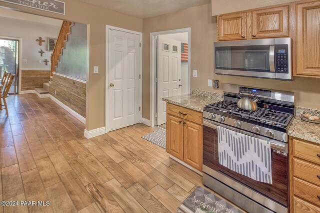 kitchen featuring light stone countertops, appliances with stainless steel finishes, a textured ceiling, and light hardwood / wood-style flooring