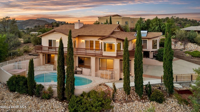 back house at dusk featuring a fenced in pool, a patio area, and a balcony