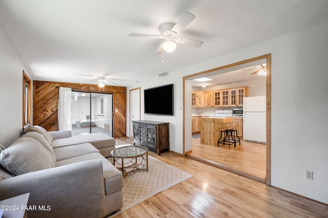 living room with light hardwood / wood-style floors, ceiling fan, and wood walls