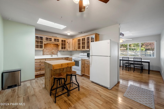 kitchen with light wood-type flooring, a skylight, white appliances, sink, and a center island