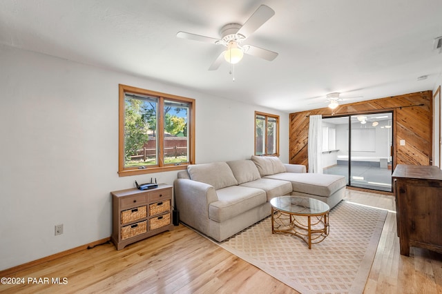 living room featuring light hardwood / wood-style flooring, ceiling fan, and wooden walls