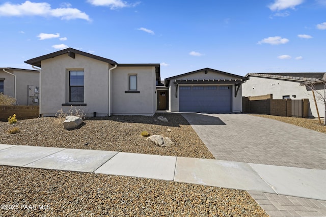 ranch-style home featuring decorative driveway, fence, a garage, and stucco siding