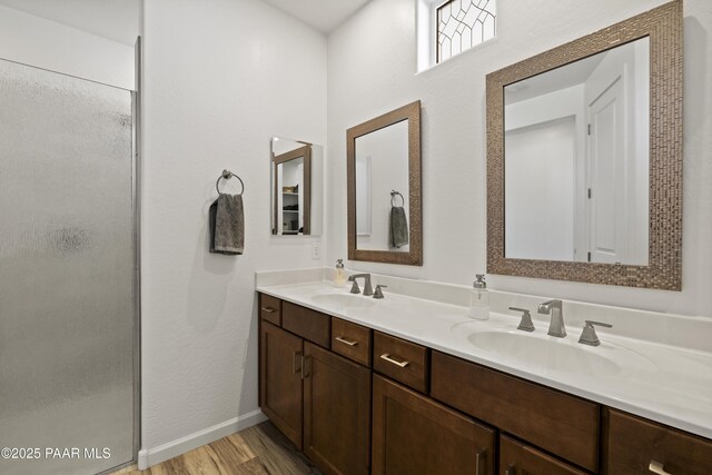 bathroom featuring a sink, a stall shower, wood finished floors, and double vanity