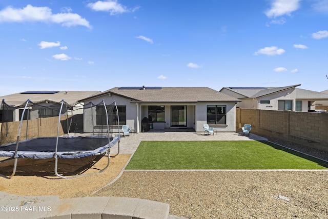 rear view of house featuring a patio, a trampoline, a fenced backyard, and stucco siding