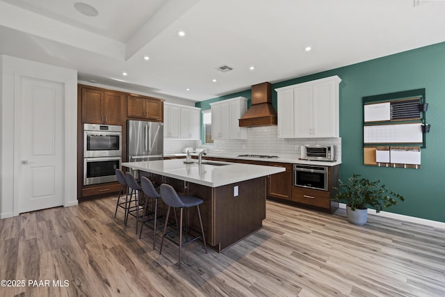 kitchen with visible vents, a breakfast bar, custom range hood, stainless steel appliances, and a sink