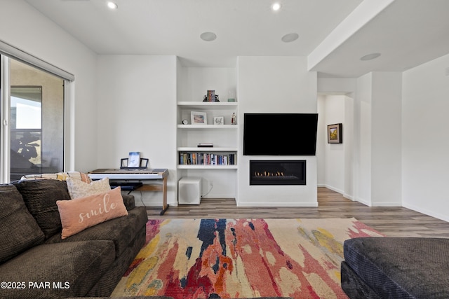 living room featuring recessed lighting, baseboards, wood finished floors, and a glass covered fireplace