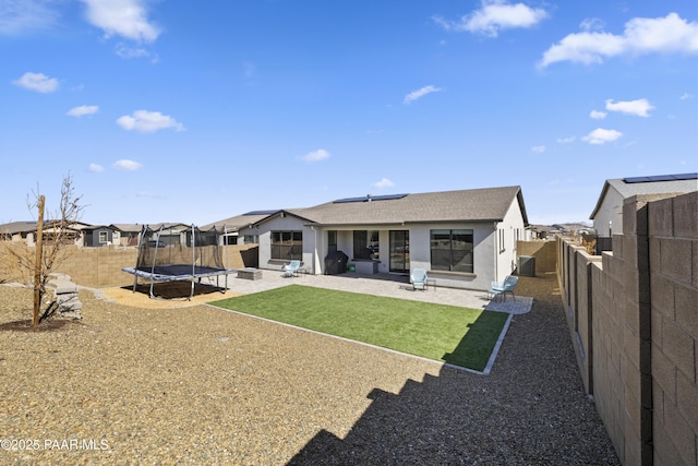 back of property with stucco siding, a trampoline, a fenced backyard, solar panels, and a patio area