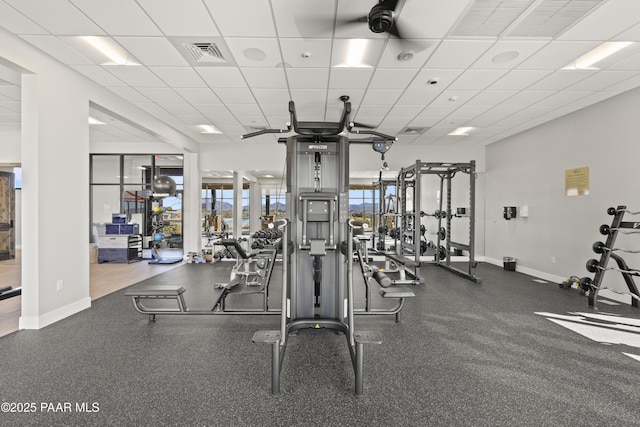 exercise room featuring visible vents, a paneled ceiling, and baseboards