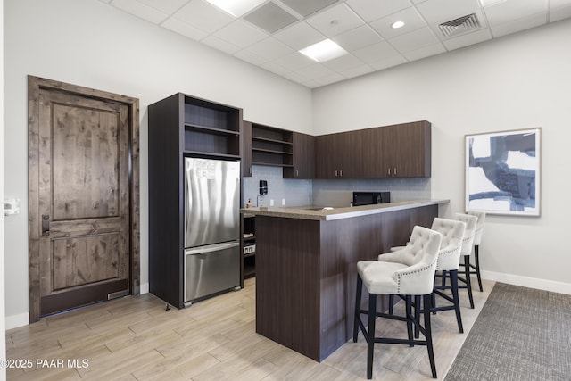 kitchen with visible vents, backsplash, a kitchen bar, freestanding refrigerator, and open shelves