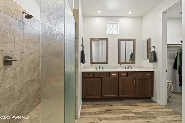 bathroom with a sink, double vanity, wood finished floors, and tiled shower