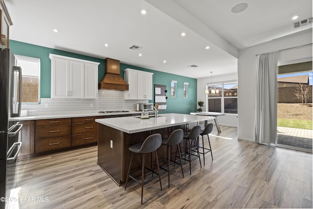 kitchen with visible vents, backsplash, freestanding refrigerator, and custom range hood