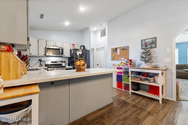 kitchen featuring kitchen peninsula, appliances with stainless steel finishes, vaulted ceiling, white cabinets, and dark hardwood / wood-style floors