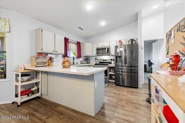 kitchen with kitchen peninsula, stainless steel appliances, vaulted ceiling, light hardwood / wood-style flooring, and white cabinetry