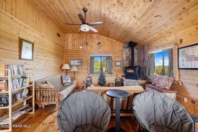 living room with vaulted ceiling, light hardwood / wood-style flooring, a wood stove, and wood walls