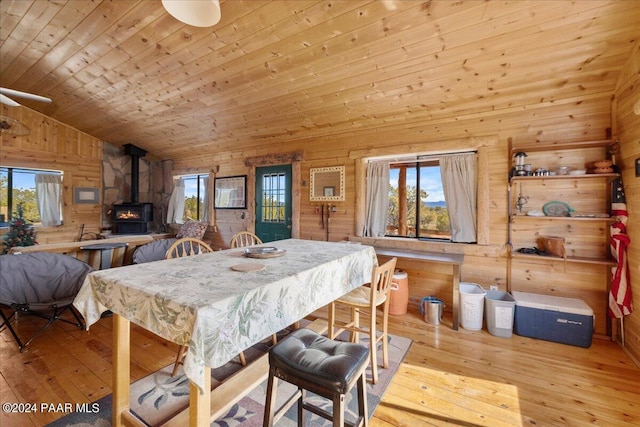 dining room with a wood stove, light hardwood / wood-style flooring, plenty of natural light, and wood walls