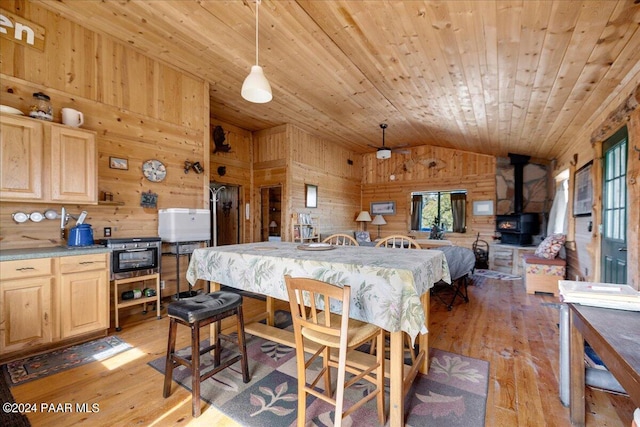 dining space with a wood stove, wooden walls, lofted ceiling, and light wood-type flooring