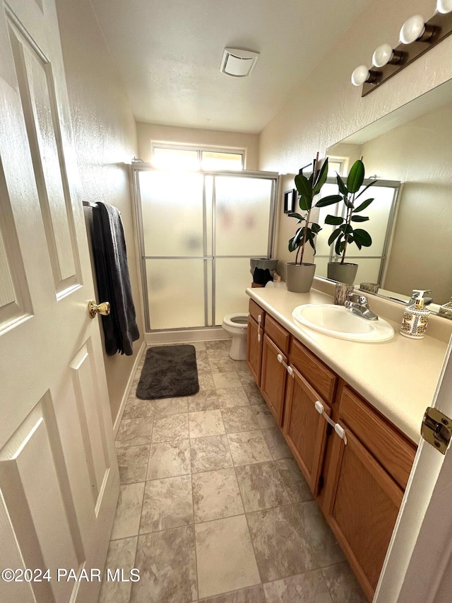 bathroom featuring vanity, a shower with shower door, and toilet