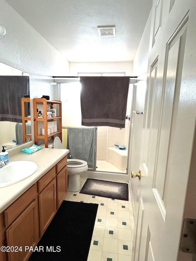 bathroom featuring a textured ceiling, tile patterned floors, a shower with door, vanity, and toilet