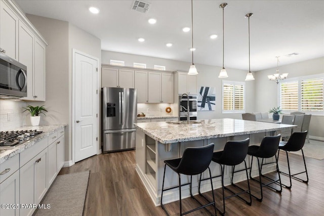 kitchen featuring visible vents, decorative backsplash, a center island with sink, dark wood-type flooring, and stainless steel appliances