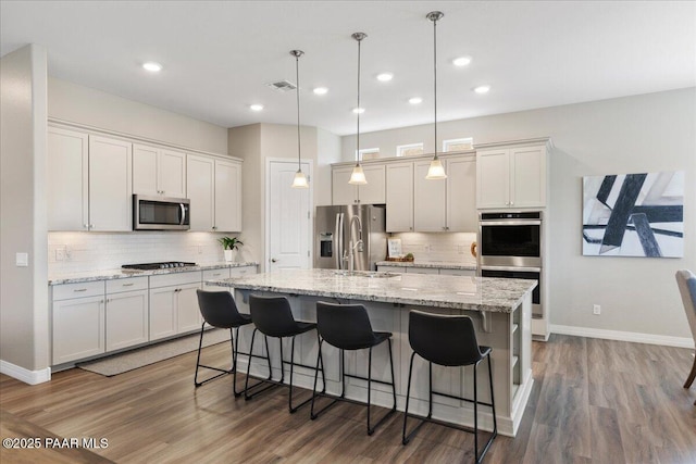 kitchen with backsplash, a center island with sink, baseboards, stainless steel appliances, and light wood-style flooring