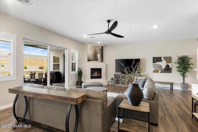 living area featuring visible vents, wood finished floors, baseboards, a large fireplace, and a ceiling fan