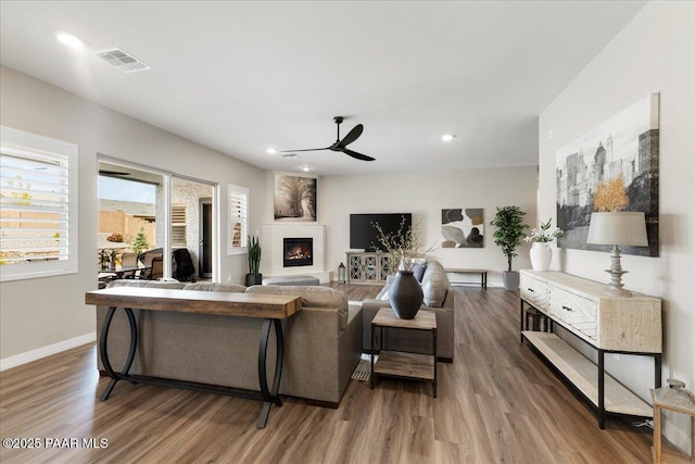 living room featuring ceiling fan, a fireplace, wood finished floors, and visible vents