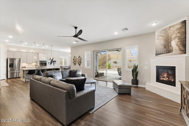 living area featuring ceiling fan, visible vents, a tiled fireplace, dark wood-style floors, and recessed lighting