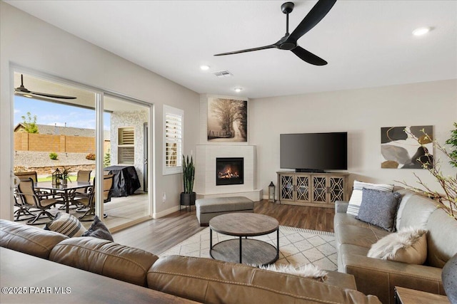 living area with ceiling fan, visible vents, wood finished floors, a glass covered fireplace, and recessed lighting