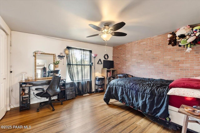 bedroom featuring hardwood / wood-style floors, ceiling fan, and brick wall