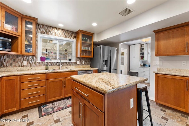 kitchen featuring a center island, appliances with stainless steel finishes, sink, and light stone counters