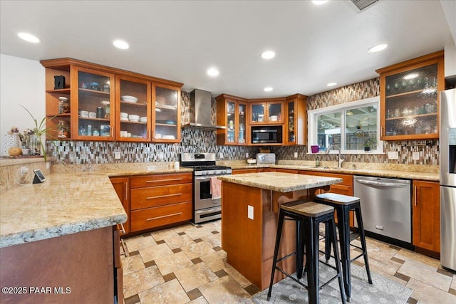 kitchen with wall chimney exhaust hood, a breakfast bar, sink, appliances with stainless steel finishes, and light stone countertops