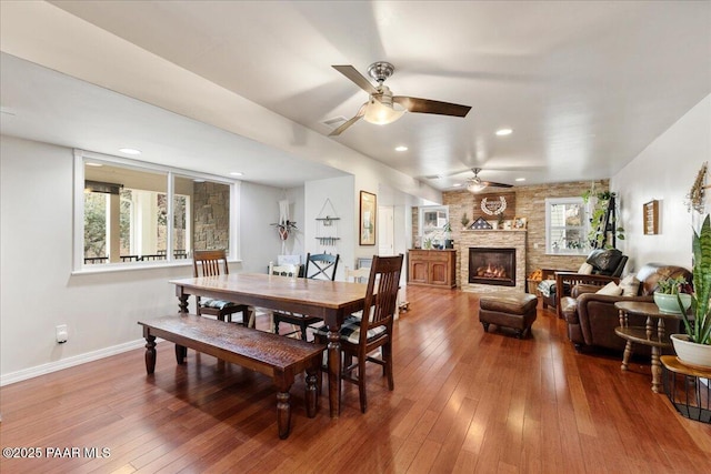 dining room featuring hardwood / wood-style flooring, a large fireplace, and ceiling fan