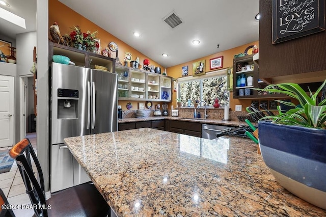 kitchen featuring kitchen peninsula, light stone counters, stainless steel appliances, vaulted ceiling, and sink