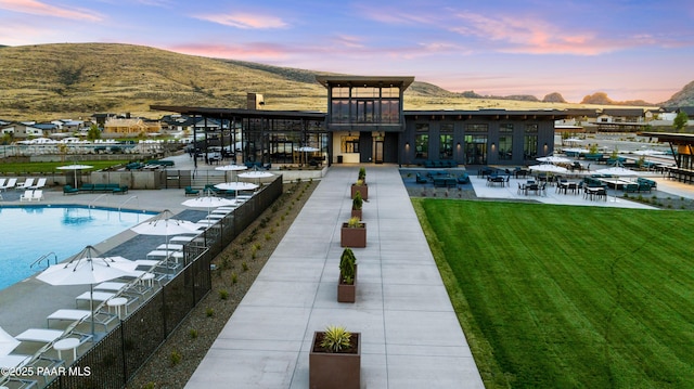 back house at dusk with a mountain view, a patio area, a community pool, and a lawn