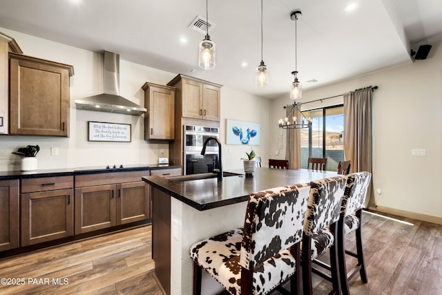 kitchen featuring wall chimney exhaust hood, sink, decorative light fixtures, a kitchen breakfast bar, and an island with sink