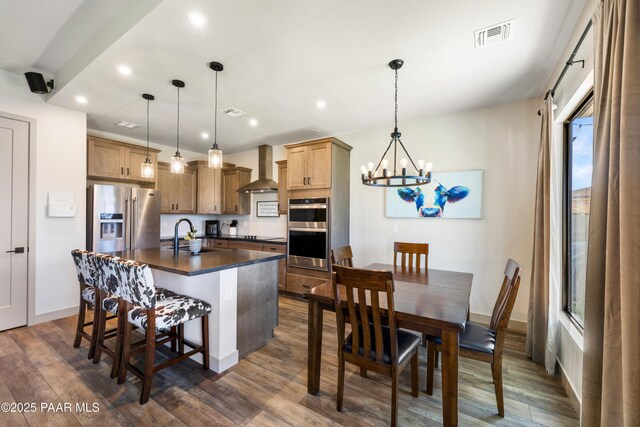 kitchen featuring wall chimney exhaust hood, appliances with stainless steel finishes, hanging light fixtures, and a center island with sink