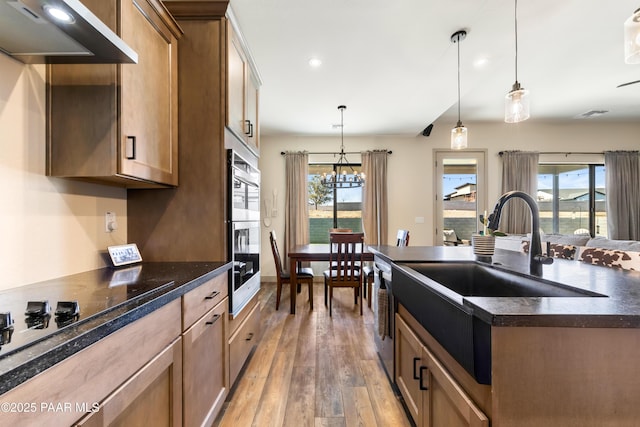 kitchen featuring decorative light fixtures, wood-type flooring, a center island, plenty of natural light, and wall chimney range hood