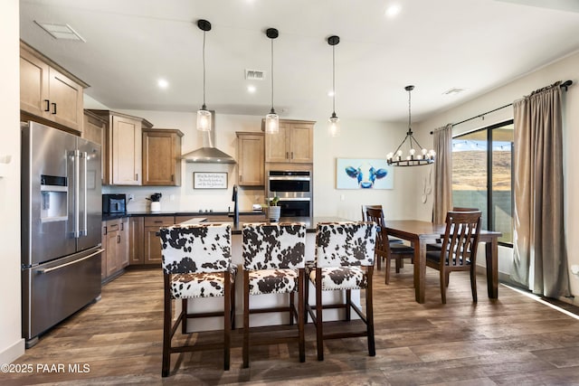 kitchen with pendant lighting, a breakfast bar area, appliances with stainless steel finishes, dark hardwood / wood-style floors, and wall chimney exhaust hood