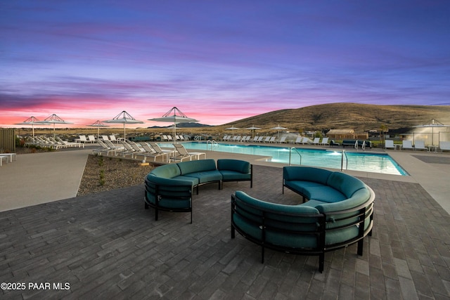 patio terrace at dusk with a community pool, a mountain view, and an outdoor living space