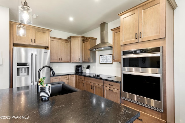 kitchen with wall chimney exhaust hood, sink, hanging light fixtures, dark stone countertops, and stainless steel appliances